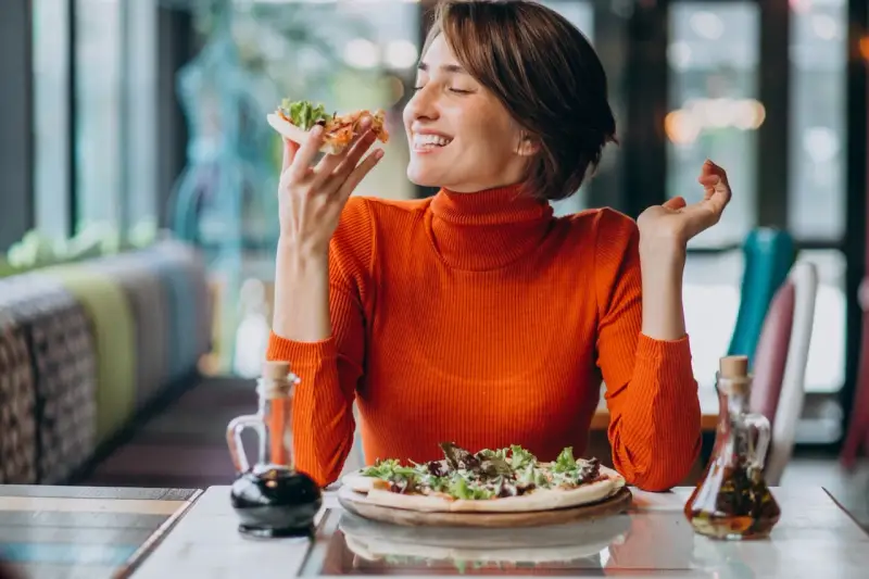 Kobieta w pomarańczowym golfie cieszy się pizzą, czując radość. W czym jest serotonina? W takich chwilach szczęścia!